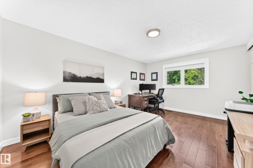 Bedroom featuring wood-finish flooring, a contemporary ceiling light fixture, a window with white trim, and light-toned walls - 15146 Ramsay Crescent, Edmonton, AB 