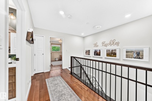 Hardwood flooring extending through a bright hallway, featuring recessed lighting and a black metal railing - 15146 Ramsay Crescent, Edmonton, AB 