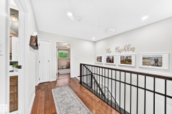 Hardwood flooring extending through a bright hallway, featuring recessed lighting and a black metal railing - 