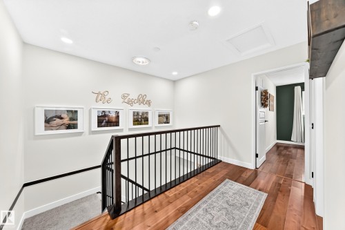 Upper-level landing featuring wood-finish flooring, recessed lighting, a modern black metal railing, and a framed doorway - 15146 Ramsay Crescent, Edmonton, AB 