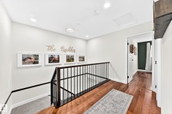 Upper-level landing featuring wood-finish flooring, recessed lighting, a modern black metal railing, and a framed doorway - 