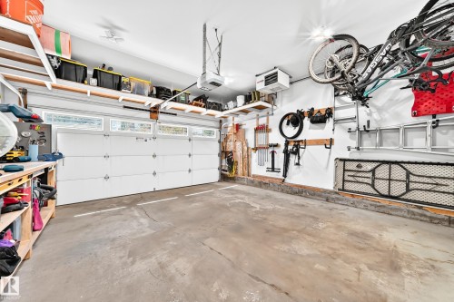 Concrete-floored garage featuring a segmented white garage door with upper window panels, overhead storage shelving, and wall-mounted organization systems - 15146 Ramsay Crescent, Edmonton, AB 
