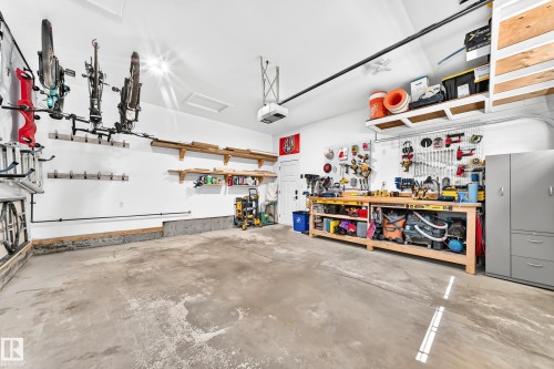 Spacious garage featuring a concrete floor, built-in shelving, wall-mounted storage solutions, and a dedicated workbench area with ample counter space - 15146 Ramsay Crescent, Edmonton, AB 