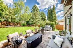 Expansive backyard featuring a large paved patio, terraced landscaping, mature trees, and a well-maintained lawn - 