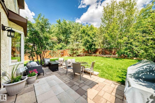 Expansive backyard featuring a stone paver patio, lush green lawn, mature trees, and a privacy fence - 15146 Ramsay Crescent, Edmonton, AB 