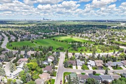 Expansive aerial perspective showcasing a residential area with mature tree-lined streets, a large central green space, and distant city skyline - 
