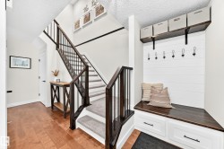 Entryway featuring wood-finish flooring, a carpeted staircase with dark wood newel posts and railings, and a built-in bench with storage drawers - 