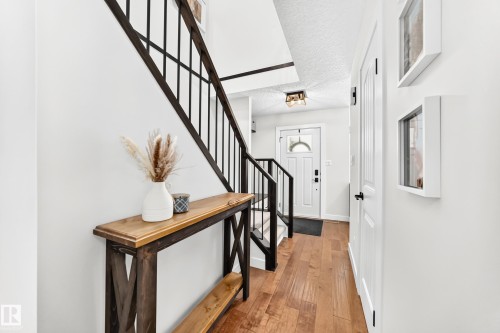 Foyer featuring wood-finish flooring, a white paneled entry door with an arched glass insert, and a staircase with black metal balusters and a wood handrail - 15146 Ramsay Crescent, Edmonton, AB 