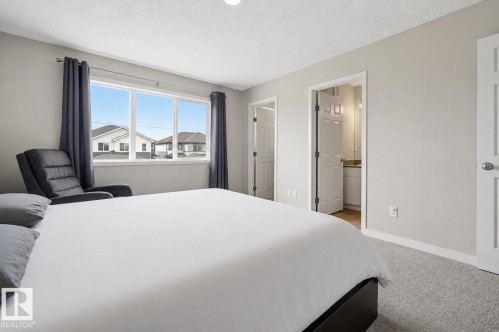 Bedroom featuring a large window, light gray walls, light-colored carpet, and two interior doors - 56 Springbrook Wynd, Spruce Grove, AB - Indoor Photo Showing Bedroom