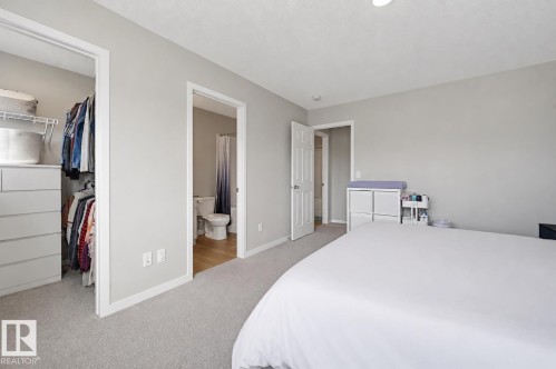 Carpeted bedroom featuring light gray walls, an open closet with built-in drawers, and a doorway revealing a bathroom with wood-finish flooring and a toilet - 56 Springbrook Wynd, Spruce Grove, AB - Indoor Photo Showing Bedroom