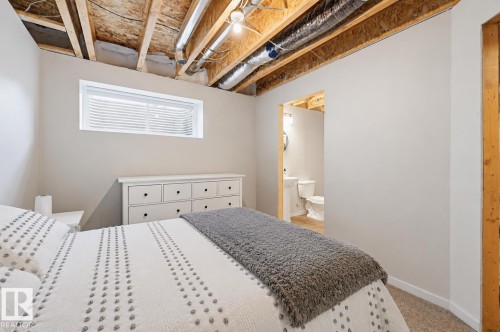 Carpeted room featuring a white-framed window with blinds, light gray walls, exposed wooden ceiling joists, and an open doorway revealing a bathroom with a pedestal sink and toilet - 56 Springbrook Wynd, Spruce Grove, AB - Indoor Photo Showing Bedroom