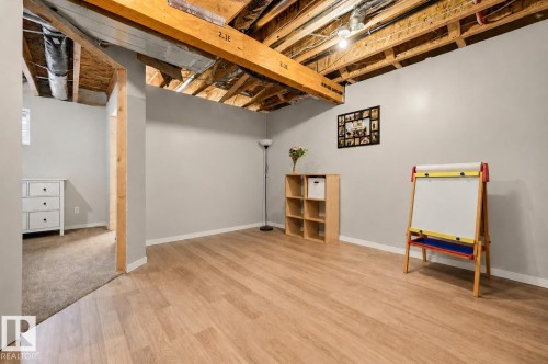 Spacious lower-level room featuring wood-finish flooring, light gray painted walls, and an open ceiling exposing structural beams and ductwork - 56 Springbrook Wynd, Spruce Grove, AB - Indoor Photo Showing Basement