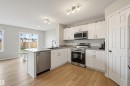 Modern kitchen featuring stainless steel appliances, white cabinetry, light-toned wood-finish flooring, a kitchen island, and a sliding glass door leading to a fenced yard - 56 Springbrook Wynd, Spruce Grove, AB  - Indoor Photo Showing Kitchen With Stainless Steel Kitchen 
