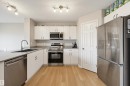 Kitchen featuring wood-finish flooring, white cabinetry, stainless steel appliances, a black undermount sink, and light countertops - 56 Springbrook Wynd, Spruce Grove, AB  - Indoor Photo Showing Kitchen With Stainless Steel Kitchen With Double Sink 