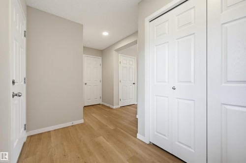Hallway featuring wood-finish flooring, light neutral wall paint, white trim, and multiple white paneled doors - 56 Springbrook Wynd, Spruce Grove, AB - Indoor Photo Showing Other Room