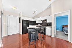 Open-concept kitchen featuring white cabinetry, black appliances, a central island with seating, and wood-finish flooring - 