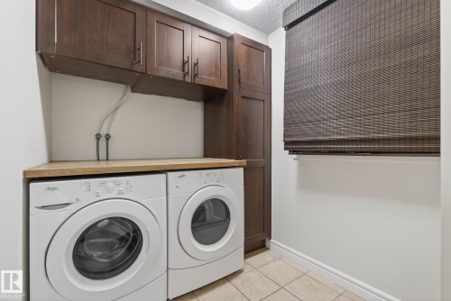 Laundry area featuring wood-finish cabinetry, a light wood-finish countertop, and neutral-toned tile flooring - 39 Meadowview Court, Spruce Grove, AB 