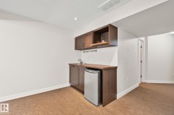 Kitchenette featuring dark wood cabinetry, a built-in stainless steel compact refrigerator, a stainless steel sink, and a wood-finish countertop - 