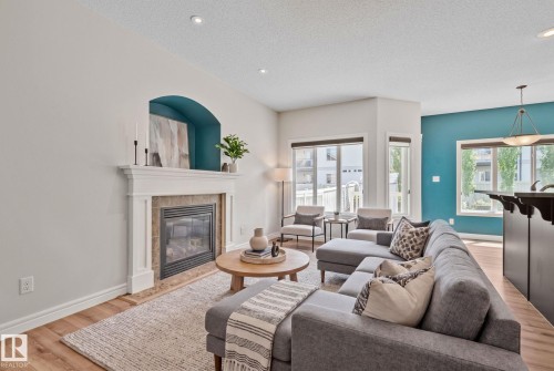 Living area featuring a fireplace with a white mantel and tile surround, recessed lighting, wood-finish flooring, multiple windows, and a distinctive accent wall - 39 Meadowview Court, Spruce Grove, AB 