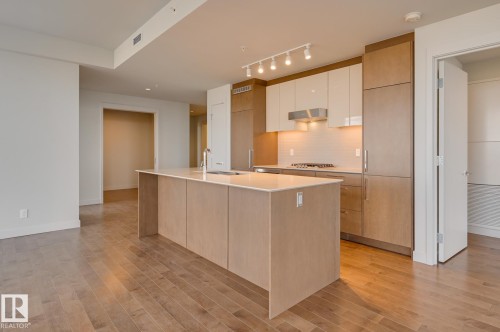 Open-concept kitchen featuring a central island with integrated sink, light-toned wood-finish cabinetry, white upper cabinets, stainless steel appliances, and wood-finish flooring - #3901 10360 102 St Nw Nw, Edmonton, AB - Indoor Photo Showing Kitchen