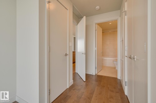 Hallway with wood-finish flooring, featuring multiple white doors with modern hardware - #3901 10360 102 St Nw Nw, Edmonton, AB - Indoor Photo Showing Other Room