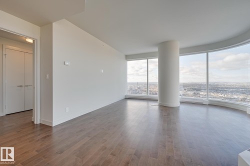 Expansive living area with curved floor-to-ceiling windows, wood-finish flooring, and a contemporary architectural column - #3901 10360 102 St Nw Nw, Edmonton, AB - Indoor Photo Showing Other Room
