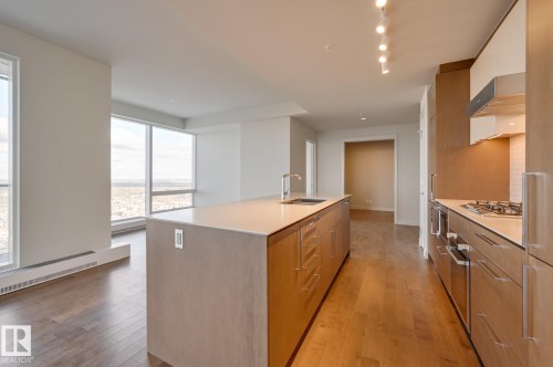 Contemporary kitchen featuring a substantial island with integrated sink, stainless steel appliances, and sleek wood-finish cabinetry - #3901 10360 102 St Nw Nw, Edmonton, AB - Indoor Photo Showing Kitchen