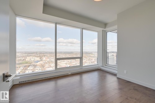 Expansive floor-to-ceiling windows with panoramic cityscape scenery, complemented by wood-finish flooring, crisp white walls, and a recessed ceiling light fixture - #3901 10360 102 St Nw Nw, Edmonton, AB - Indoor Photo Showing Other Room