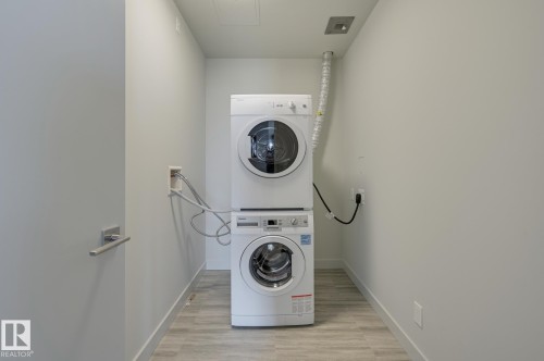 Dedicated laundry space featuring a stacked washer and dryer, light-toned wood-finish flooring, and white walls - #3901 10360 102 St Nw Nw, Edmonton, AB - Indoor Photo Showing Laundry Room