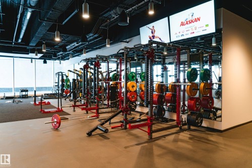 Spacious fitness area featuring multiple weight racks, floor-to-ceiling windows, recessed lighting, and dual large-format display screens - #3901 10360 102 St Nw Nw, Edmonton, AB - Indoor Photo Showing Gym Room
