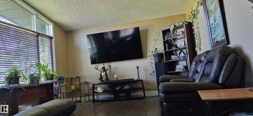 Spacious living area featuring wood-finish flooring, neutral wall tones, and a prominent window with horizontal blinds - 10523 105 Street, Westlock, AB 