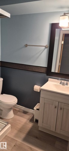 Bathroom featuring a light wood-finish vanity with a white countertop and integrated sink, a framed mirror, and a wall-mounted light fixture - 10523 105 Street, Westlock, AB 