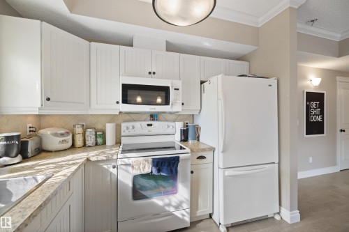 Kitchen featuring white cabinetry with dark hardware, laminate countertops, and a neutral tile backsplash - #206 10232 115 St Nw, Edmonton, AB 