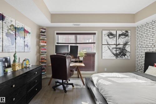 Bedroom featuring wood-finish flooring, a tray ceiling, and a window with blinds - #206 10232 115 St Nw, Edmonton, AB 