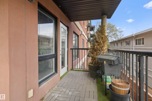 Outdoor balcony featuring a herringbone-patterned paver floor, black metal railings, and a white framed glass door - #206 10232 115 St Nw, Edmonton, AB 