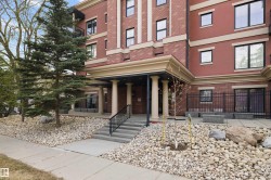 Building exterior featuring a brick facade with light-colored accent banding, a covered entryway with classical columns, and a concrete staircase with black handrails - 