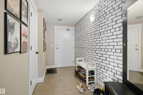 Entryway featuring a white brick-pattern accent wall, neutral-toned walls, and wood-finish flooring - #206 10232 115 St Nw, Edmonton, AB 