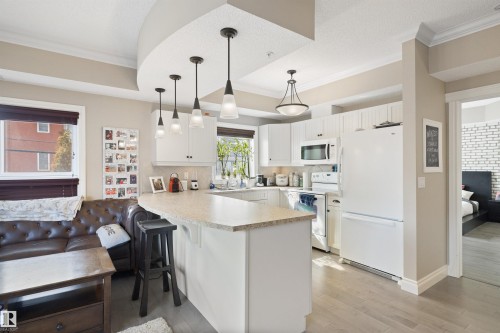 Open-concept kitchen featuring white cabinetry, light-toned countertops, and full-size appliances - #206 10232 115 St Nw, Edmonton, AB 