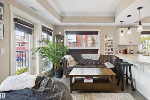 Open-concept living area featuring light wood-finish flooring, a kitchen bar with pendant lighting, and access to a balcony - #206 10232 115 St Nw, Edmonton, AB 