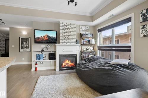 Living space featuring a fireplace with a white mantel, light brick surround, and wood-finish flooring - #206 10232 115 St Nw, Edmonton, AB 