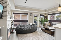 Living area featuring light wood-finish flooring, a white brick-finish fireplace with a mantel, and a tray ceiling with crown molding - 