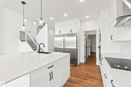White kitchen featuring a large island with an undermount sink, quartz countertops, stainless steel appliances, and wood-finish flooring - 2232 5 Avenue, Edmonton, AB 