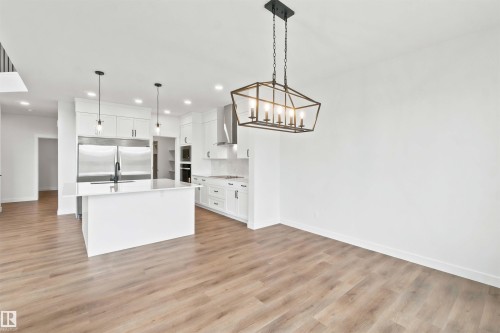 Open-concept kitchen and dining area featuring light wood-finish flooring, white cabinetry, stainless steel appliances, a central island with an undermount sink, and a black geometric chandelier - 2232 5 Avenue, Edmonton, AB 