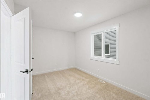 Carpeted room featuring a double-pane window with white trim, a flush-mount ceiling light, and a panel door with black hardware - 2232 5 Avenue, Edmonton, AB 