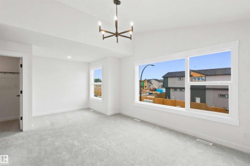 Spacious room featuring light gray carpeting, crisp white walls, a contemporary chandelier, recessed lighting, and large windows providing abundant natural light - 2232 5 Avenue, Edmonton, AB 