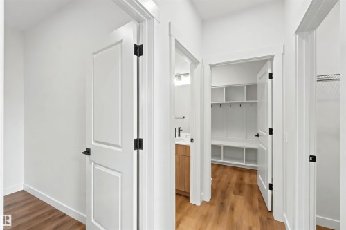 Hallway with wood-finish flooring, white paneled doors, and matte black hardware - 2232 5 Avenue, Edmonton, AB 