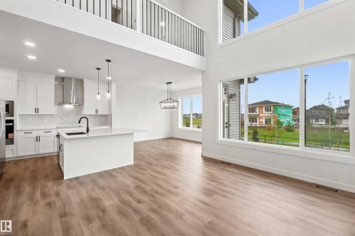 Open-concept living area featuring wood-finish flooring, a contemporary kitchen island with a black faucet, white shaker cabinetry, a stainless steel range hood, and large windows providing ample natural light - 2232 5 Avenue, Edmonton, AB 