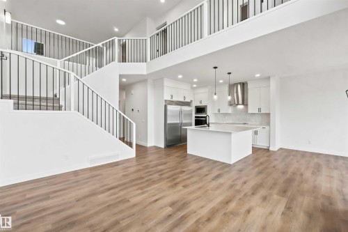 Open-concept living area featuring a modern kitchen with a large island, stainless steel appliances, and white cabinetry - 2232 5 Avenue, Edmonton, AB 