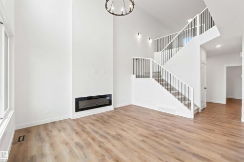Two-story living area featuring a modern linear electric fireplace, wood-finish flooring, and a contemporary chandelier - 2232 5 Avenue, Edmonton, AB 