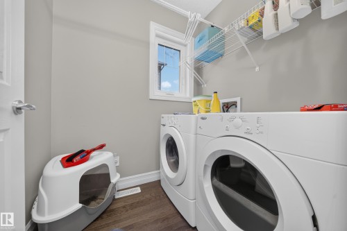 Dedicated laundry area featuring a washer and dryer, wood-finish flooring, a single window, overhead wire shelving, and a wall-mounted drying rack - 64 655 Tamarack Road, Edmonton, AB 